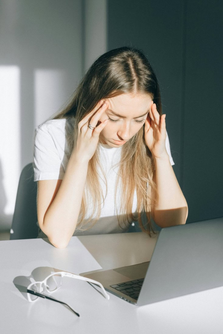Headache experienced due to stress or fatigue, woman with painful headache at table.